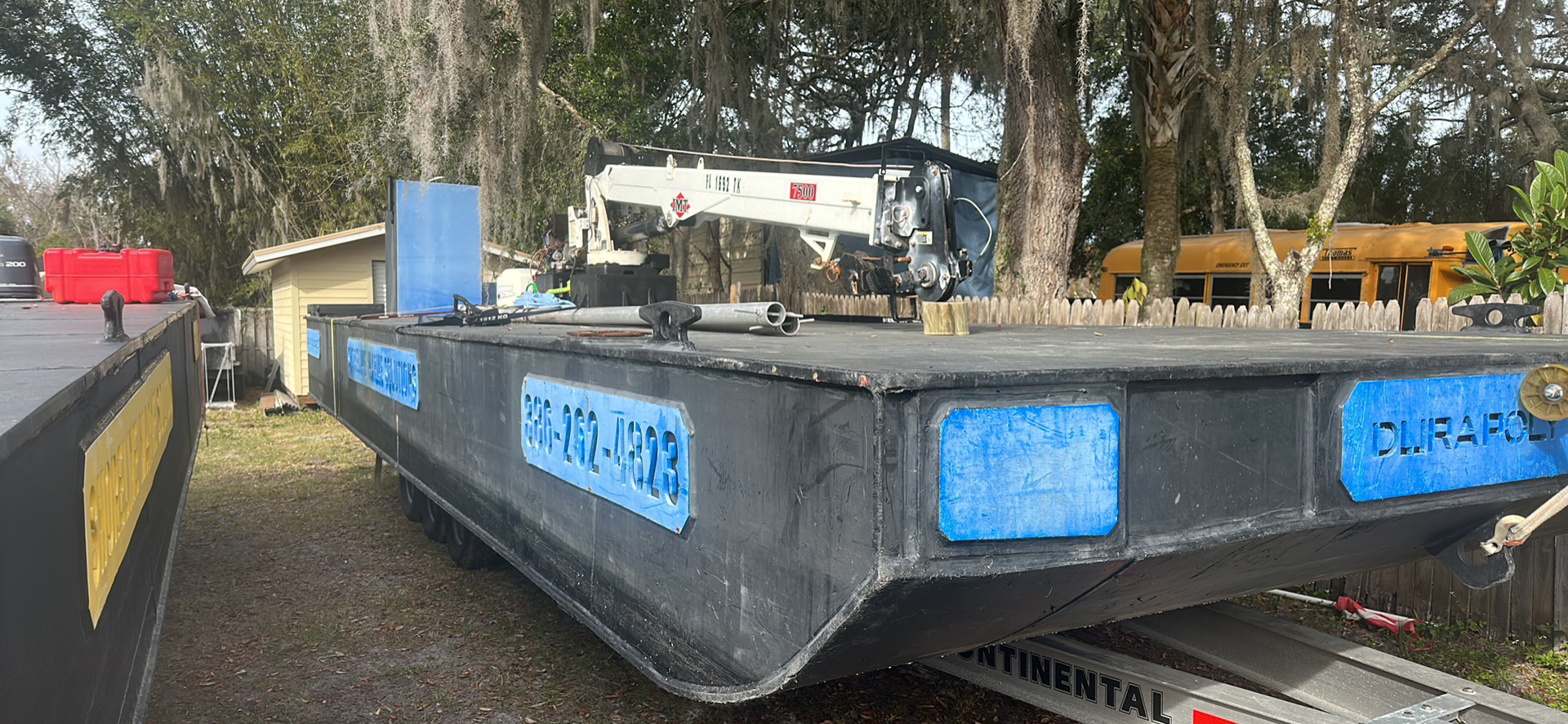 Ready to deliver Shoreline Marine Solutions barge with white crane and blue highlights on a trailer.