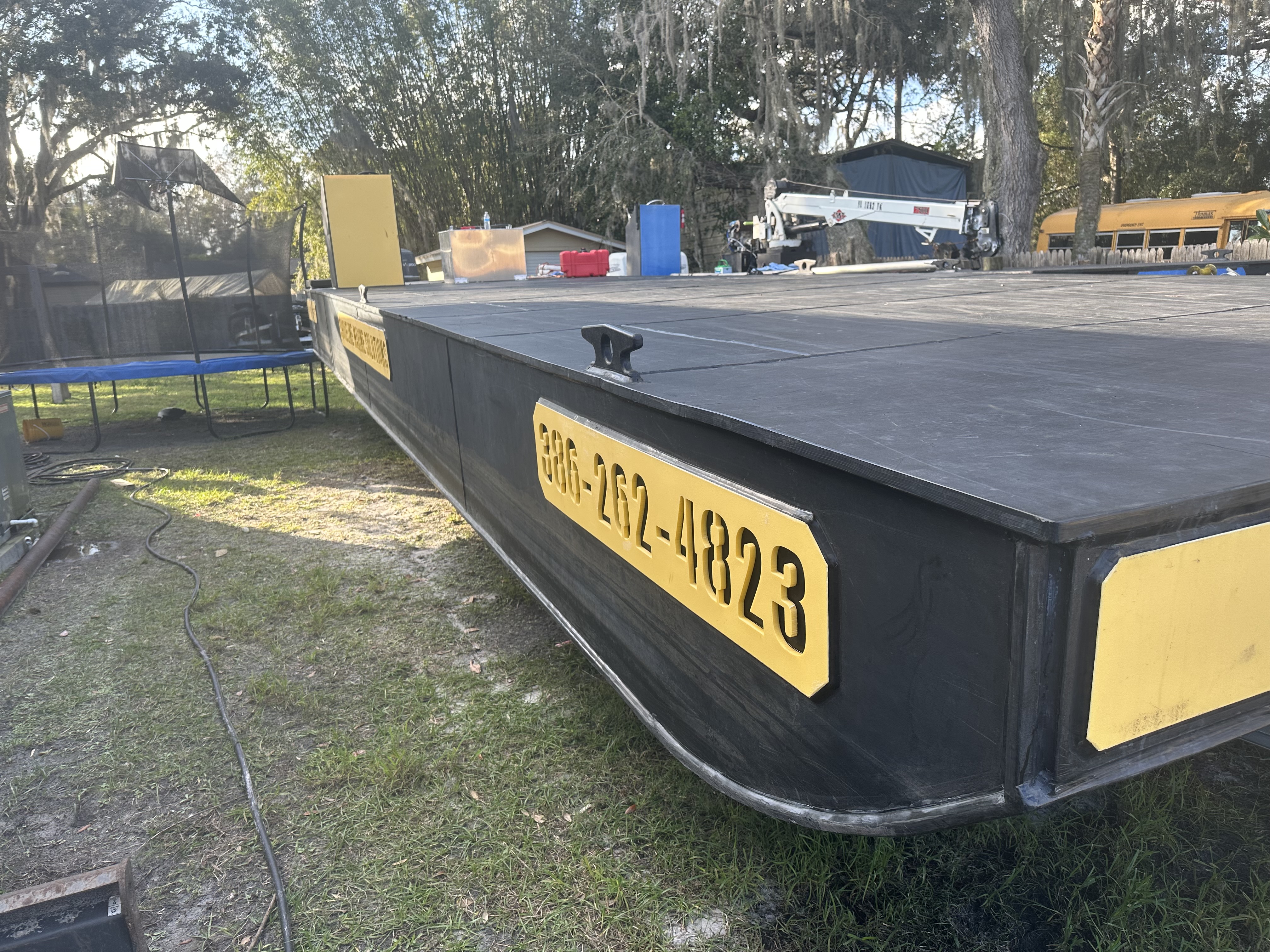 Ready to deliver Shoreline Marine Solutions barge with crane and yellow highlights on a trailer.