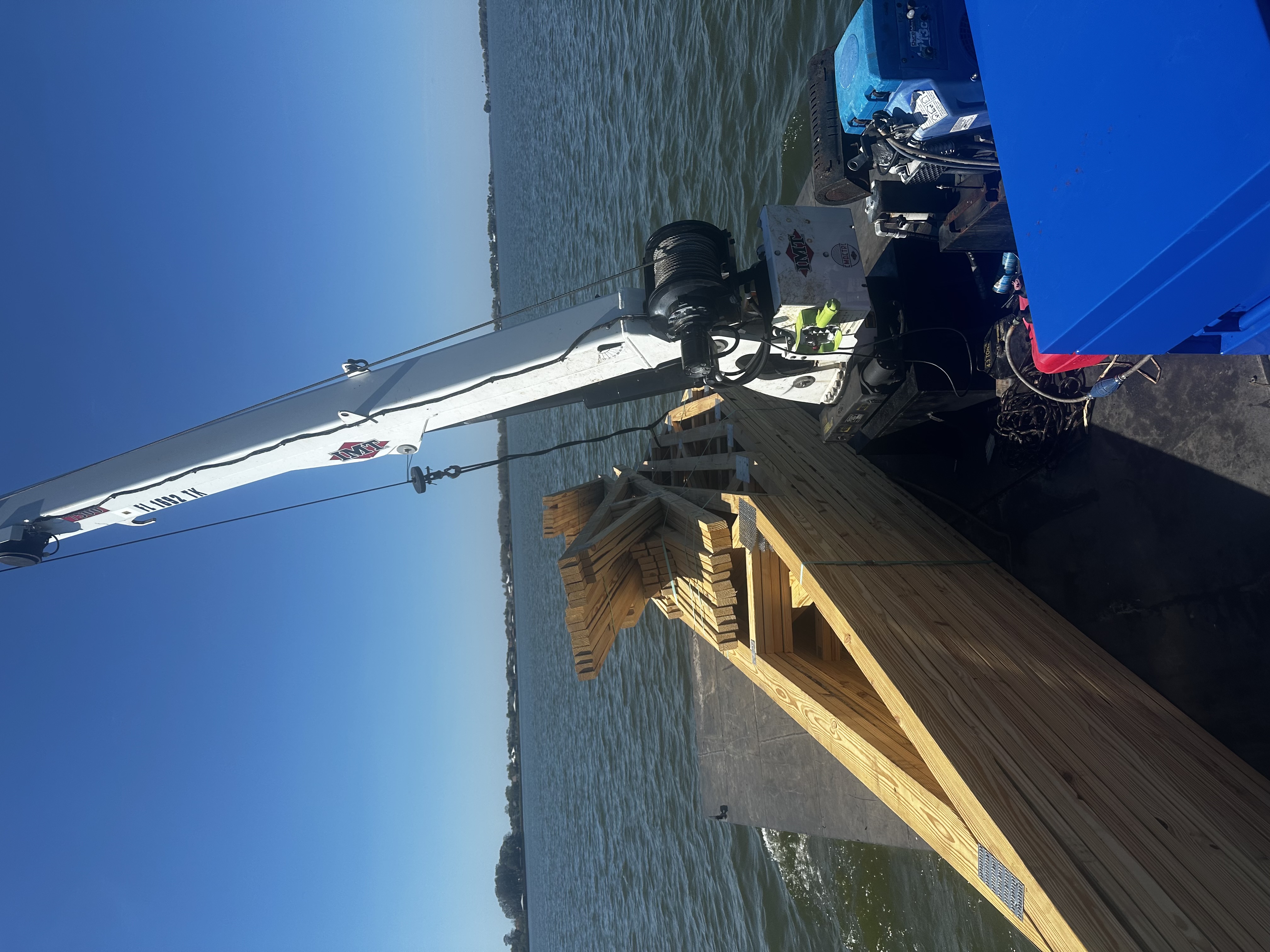 Reliable Shoreline Marine Solutions barge with attatched crane on the water with wood stored on deck.
