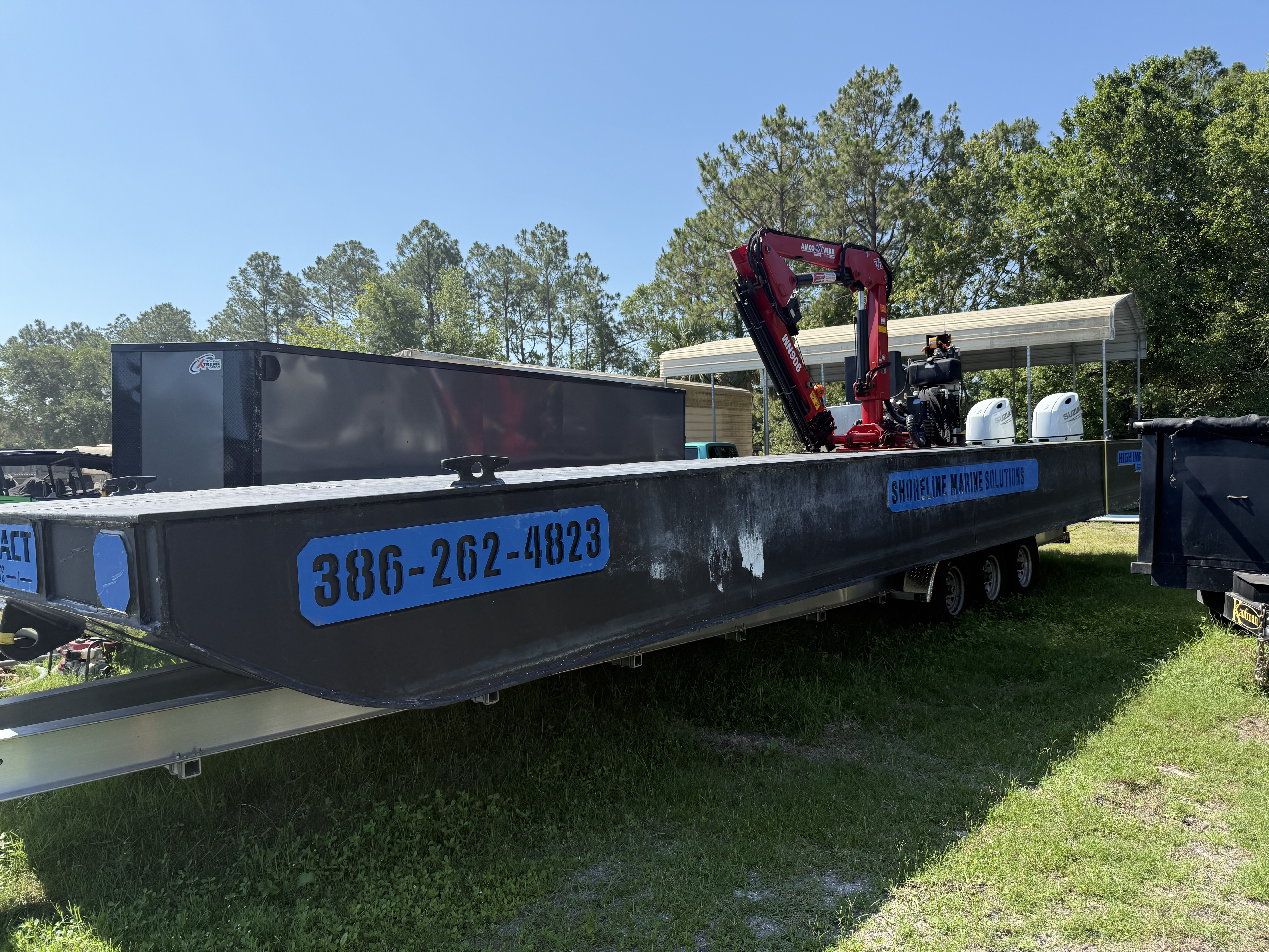 Ready to deliver Shoreline Marine Solutions barge with red crane and blue highlights on a trailer.